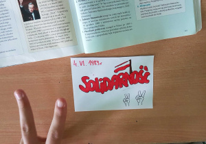 Podręcznik do historii i pokolorowana ulotki Solidarność w klasie 8b, znak zwycięstwa palcami.
