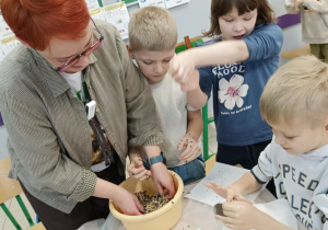 Uczniowie wraz z nauczycielem wieszają karmnik zrobiony z odpadów.