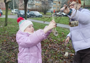 Uczniowie wraz z nauczycielem wieszają karmnik zrobiony z odpadów.
