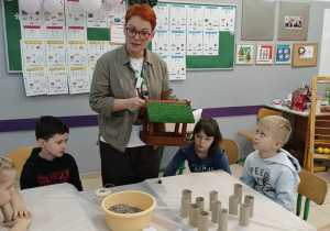 Uczniowie wraz z nauczycielem wieszają karmnik zrobiony z odpadów.