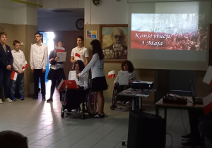 Uczniowie ubrani odświętnie prezentujący informacje w tle obraz J. Matejki, Konstytucja 3 maja 1791 roku