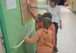 Dzieci wraz z nauczycielką przyczepiają swoje prace na tablicy.