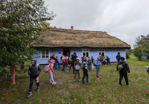 Uczniowie podczas zwiedzania Skansenu Wsi Łowickiej w Maurzycach na tle zabudowania mieszkalnego.