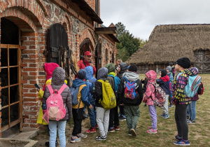 Uczniowie podczas zwiedzania Skansenu Wsi Łowickiej w Maurzycach na tle zabudowania gospodarczego.